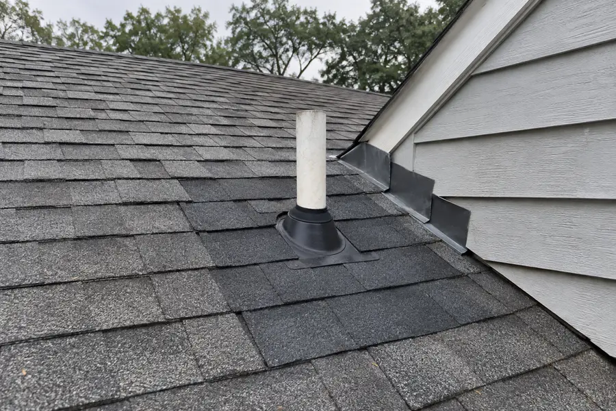 Repaired section of a shingle roof around a vent pipe with new flashing.