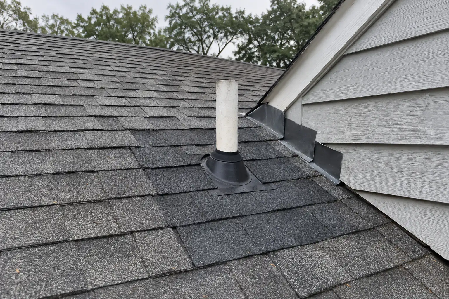 Section of a shingle roof with new replacement shingles, a new pipe boot and fresh step flashing beside a dormer.