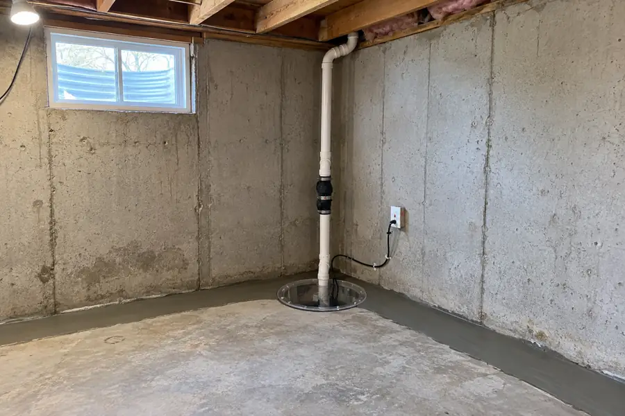 Basement corner with a new sump pit, pump discharge line and a freshly poured interior drain strip.