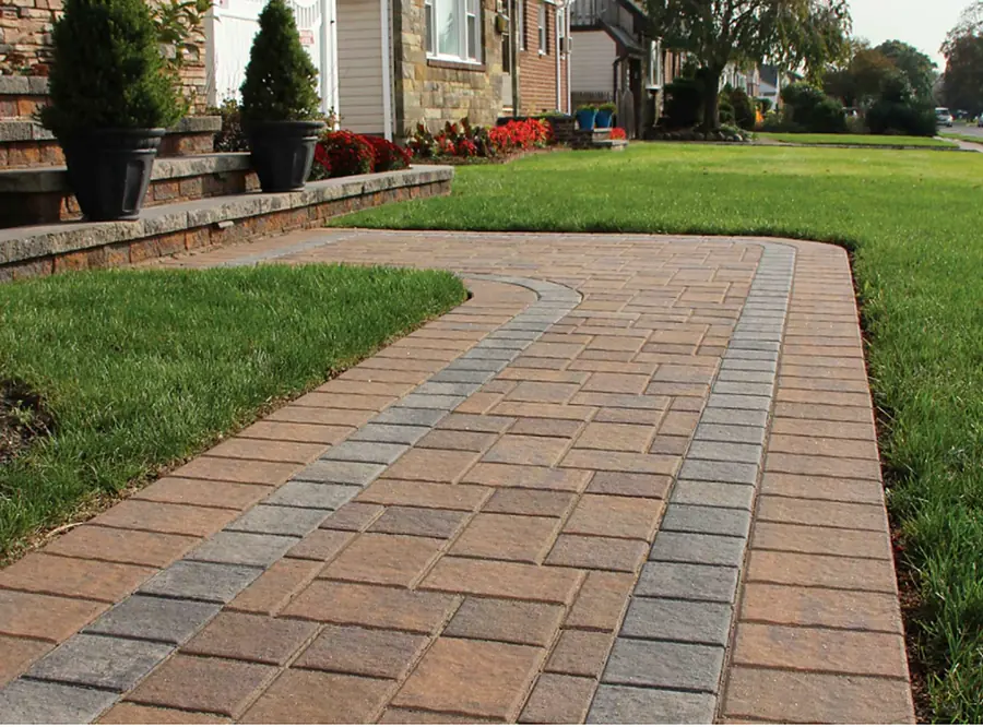 Curved paver walkway across a lawn with a low block retaining wall and planted bed behind it.