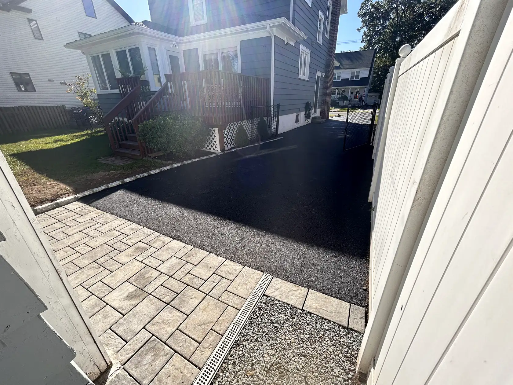 Asphalt driveway beside a paver walkway and a white vinyl fence.