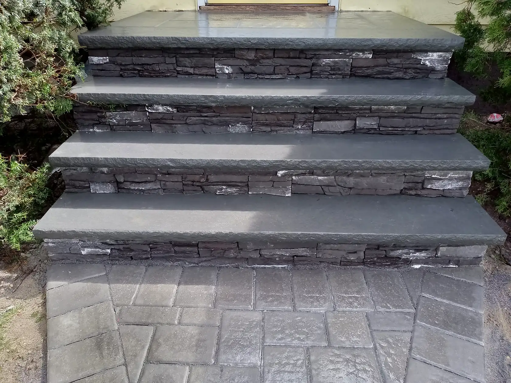 Front steps with a natural stone riser face, bluestone treads and a stamped concrete landing.