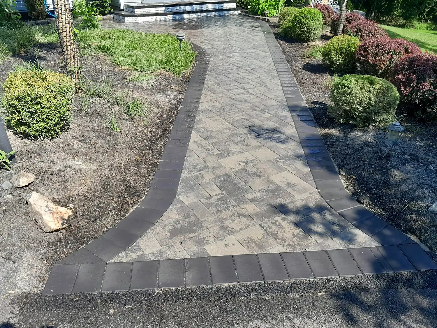 Paver walkway with a dark contrasting border running between planted beds.